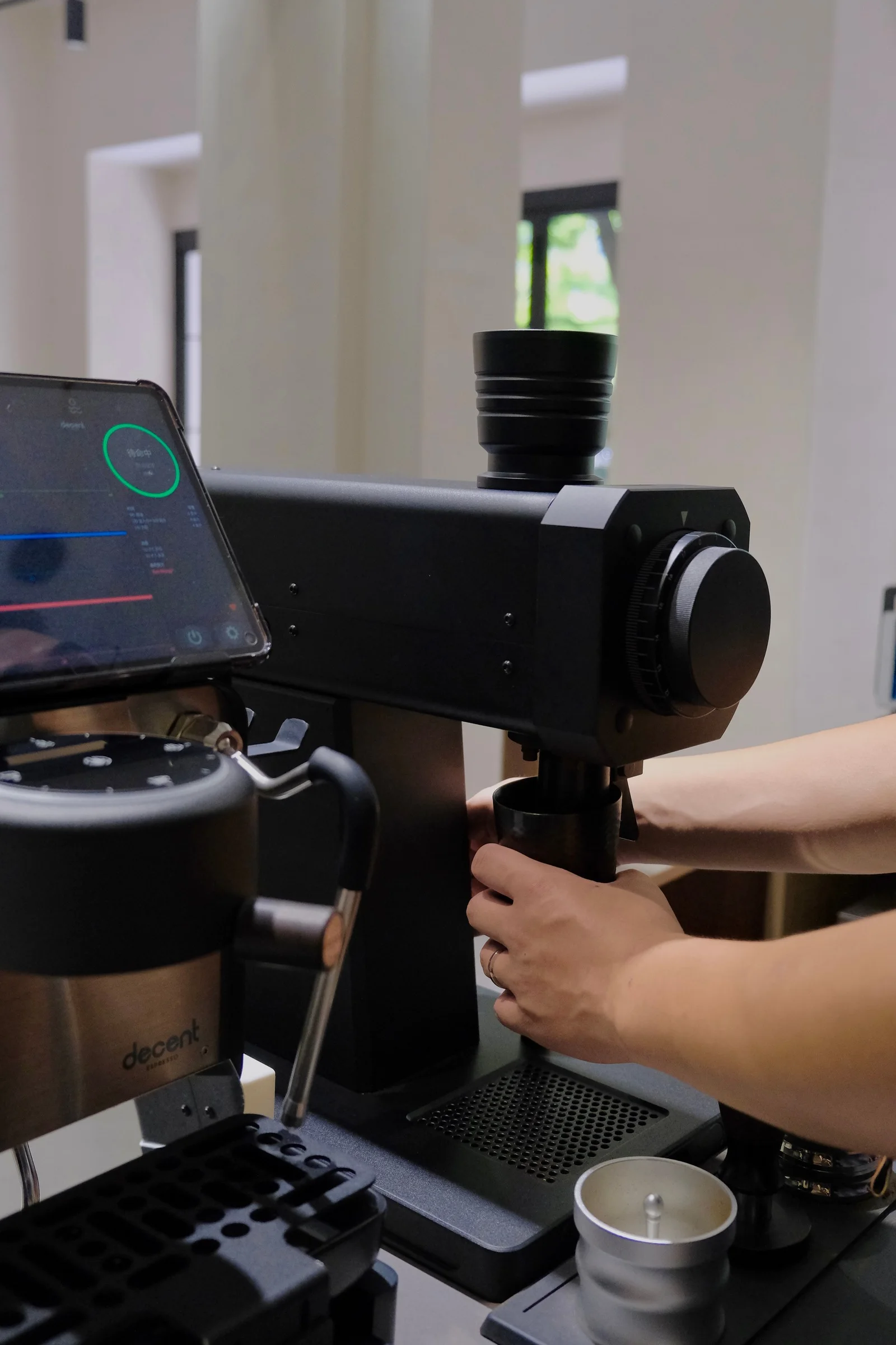 Hands holding a dosing cup beneath a black FM grinder at a coffee bar