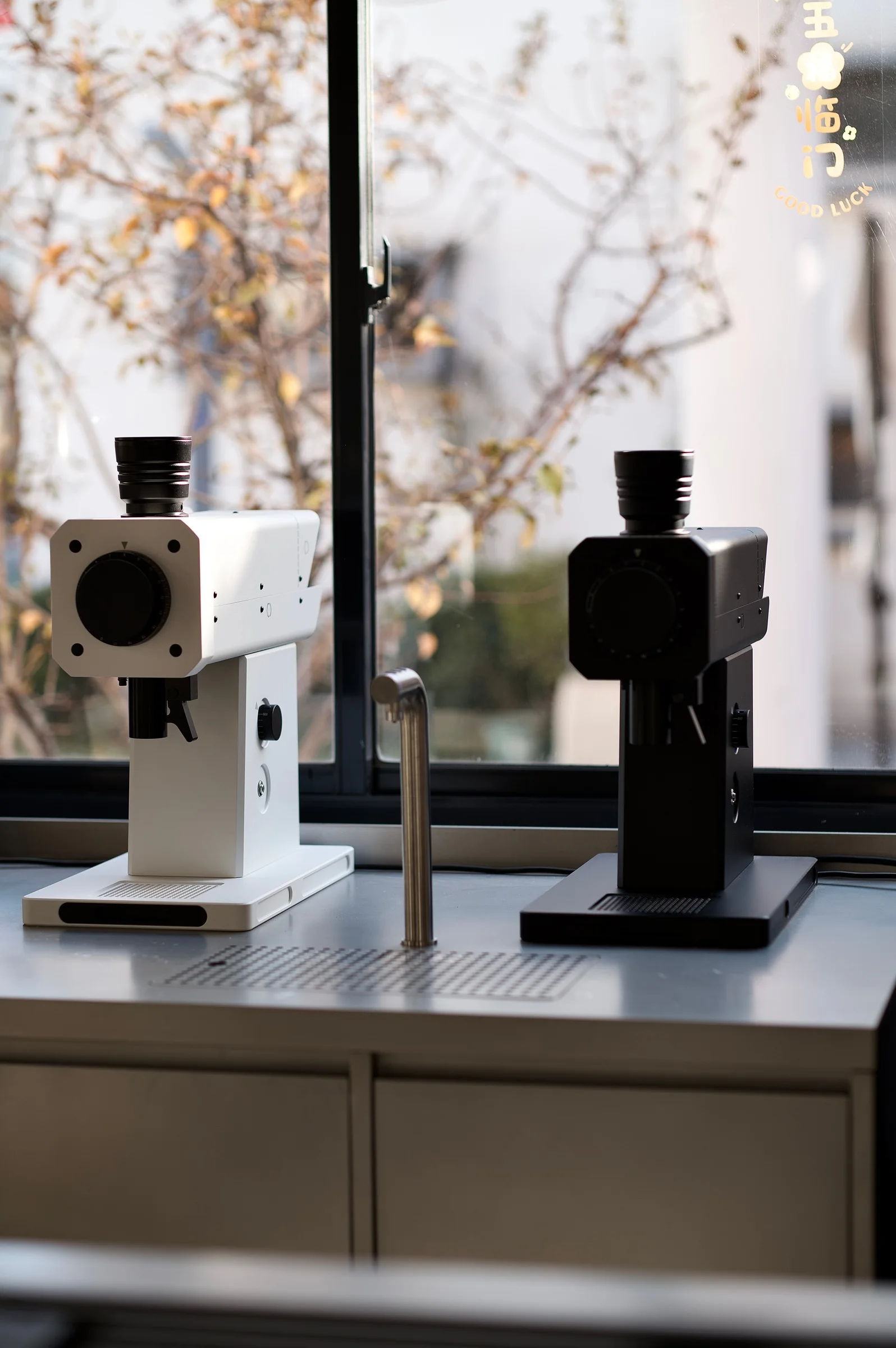 Black and white FM flat-burr grinders on a coffee bar by a window